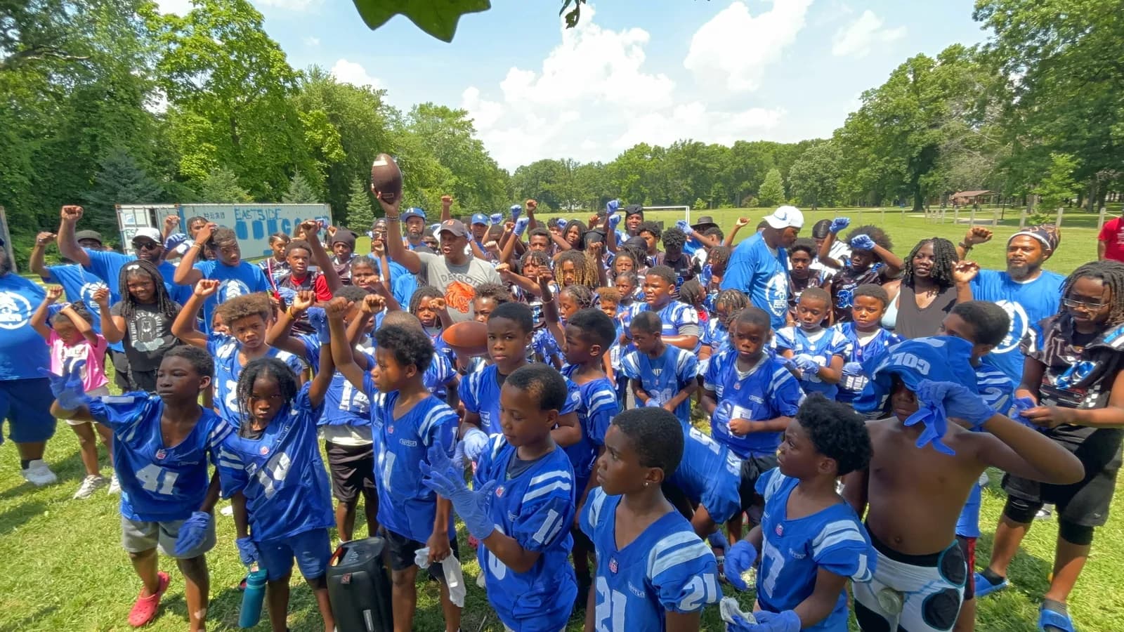 A crowd of Detroit children in Eastside Colts jerseys with their arms raised